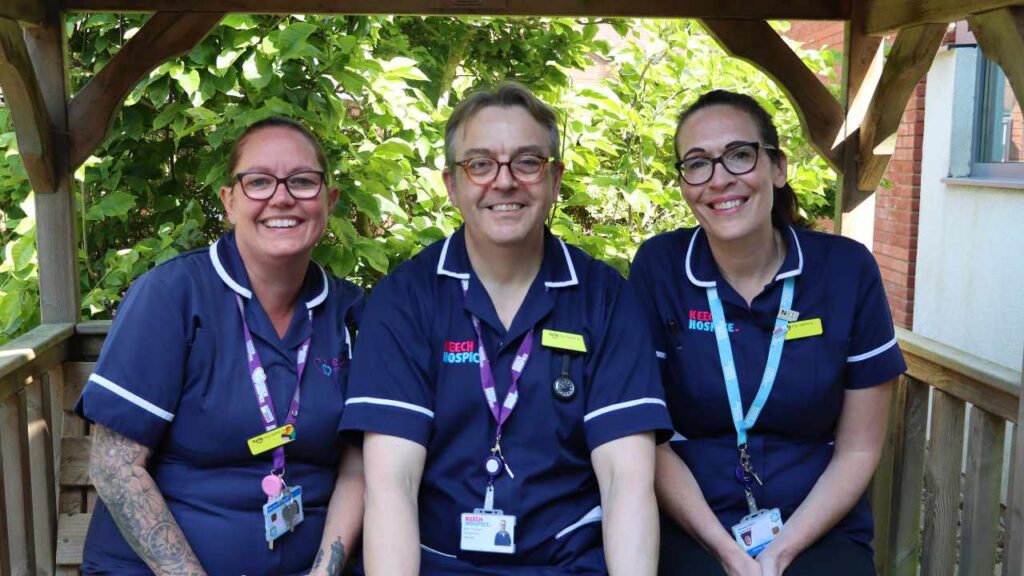 two female nurses and a male nurse smiling on a bench